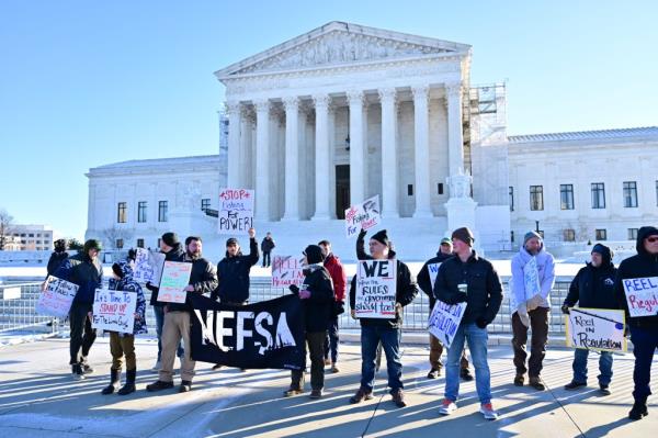 A group of people holding signs advocating for fewer regulations in the herring fishing industry in front of a white building