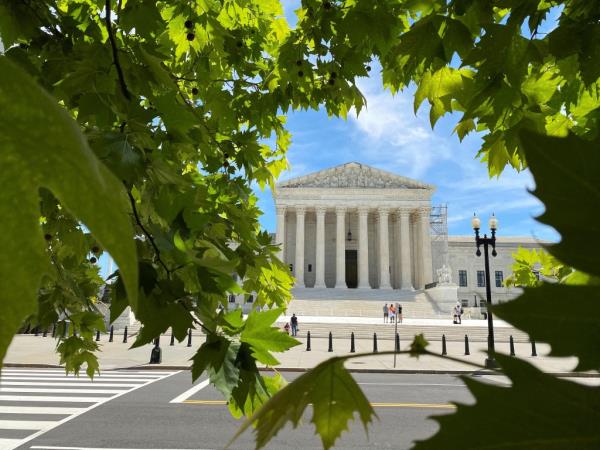 A general view of the U.S. Supreme Court building with columns, steps and people walking in front.