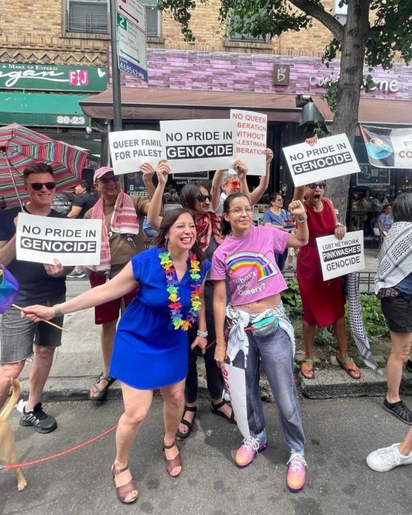 A group of people including tiffany caban in a pink t-shirt  holding signs reading 'No Pride in Genocide' and 'Queer Families for Palestine' at the Queens Pride parade.