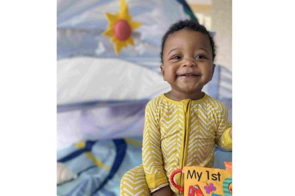 1-year-old Akil “Sonny” McLeod. winner of 2024 Gerber Baby Photo Search. smiles for the camera while wearing a yellow one-piece outfit.