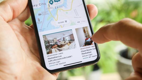 Woman in New York City booking an apartment room using Airbnb app on her phone displaying a map