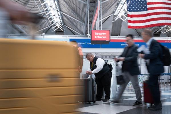 Passengers passing through O'Hare airport during the Independence Day holiday travel week in 2024 with a man standing next to luggage.