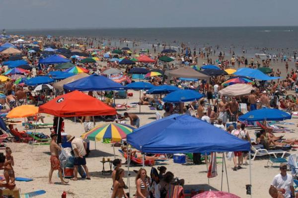 Crowded beach on Independence Day with beachgoers and packed tents, people using umbrellas under hot and humid weather conditions