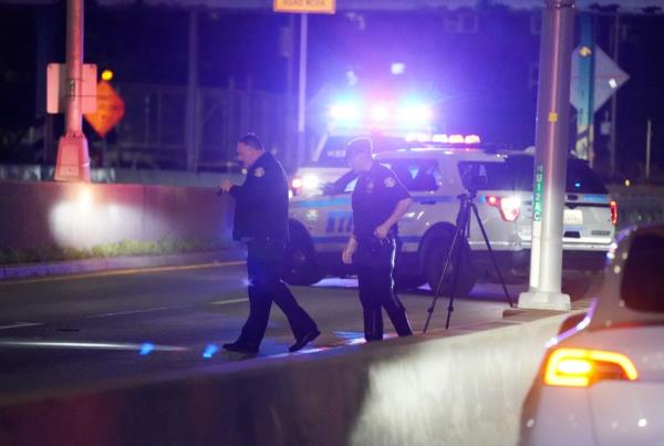 police at the scene with a patrol car with flashign lights behind them